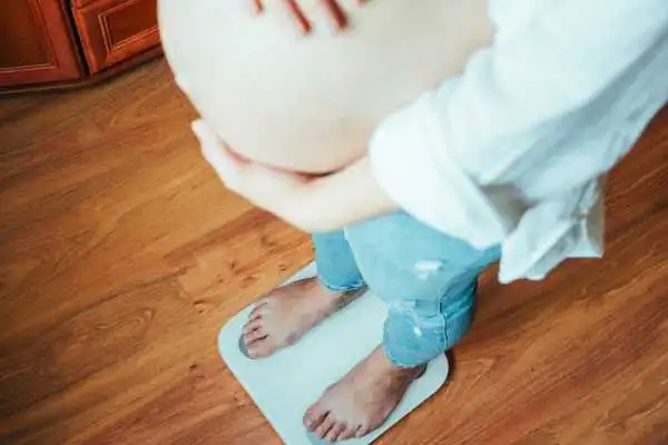 Image of woman weighing herself and experiencing weight gain through pregnancy Loughborouogh